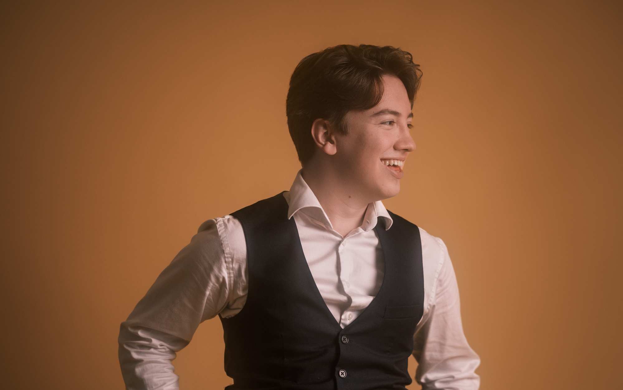 Nuori mies seisoo hymyillen kellertävää taustaa vasten. Hän katsoo oikealle pois päin kamerasta.